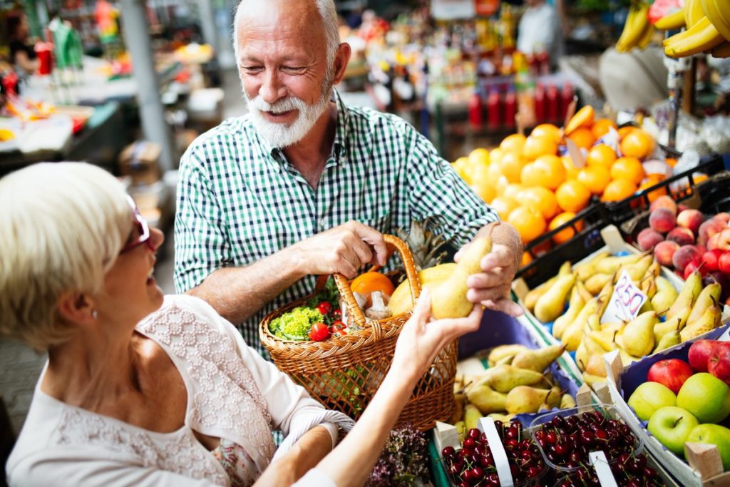 Ein älteres Paar kauft gutgelaunt auf einem Markt ein