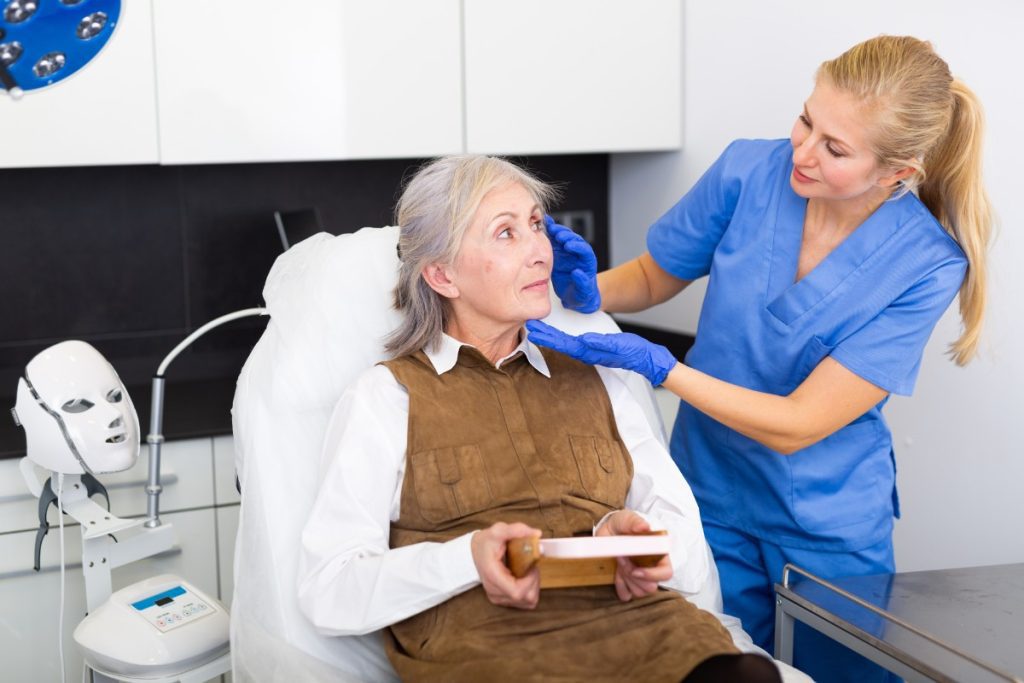 Eine Krankenschwester, die sich um eine ältere Dame auf einem Behandlungsstuhl kümmert