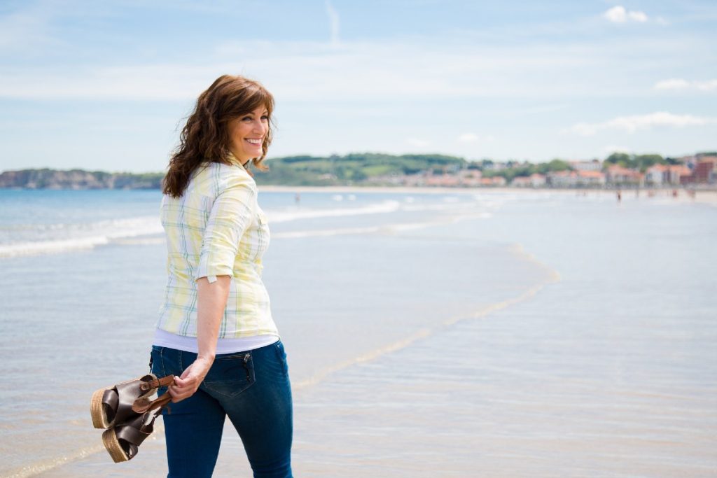 Frau spaziert am Strand mit Ihren Sandalen in der Hand