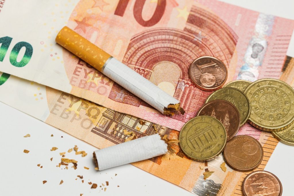 Zerbrochene Zigarette auf Münzen und Geldscheinen liegend