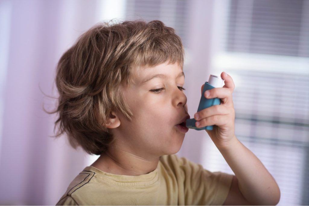 Kleiner Junge, der sich mit einem Inhaler Asthmaspray zuführt