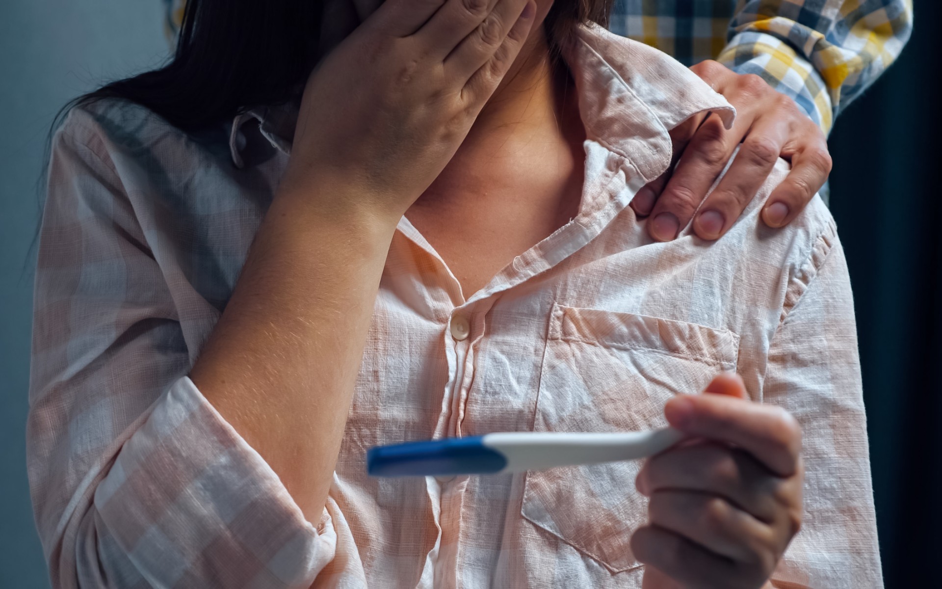 Junge Frau, die mit der Hand vor dem Mund auf einen Schwangerschaftstest schaut