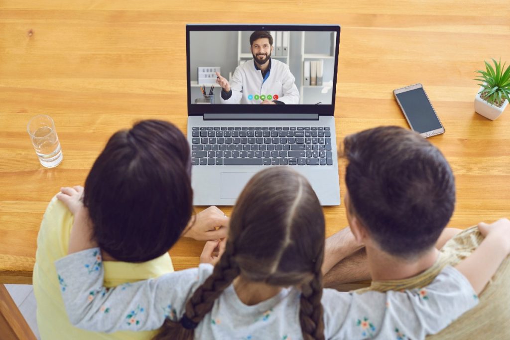 Eine dreiköpfige Familie im Videogespräch mit ihrem Arzt über Laptop