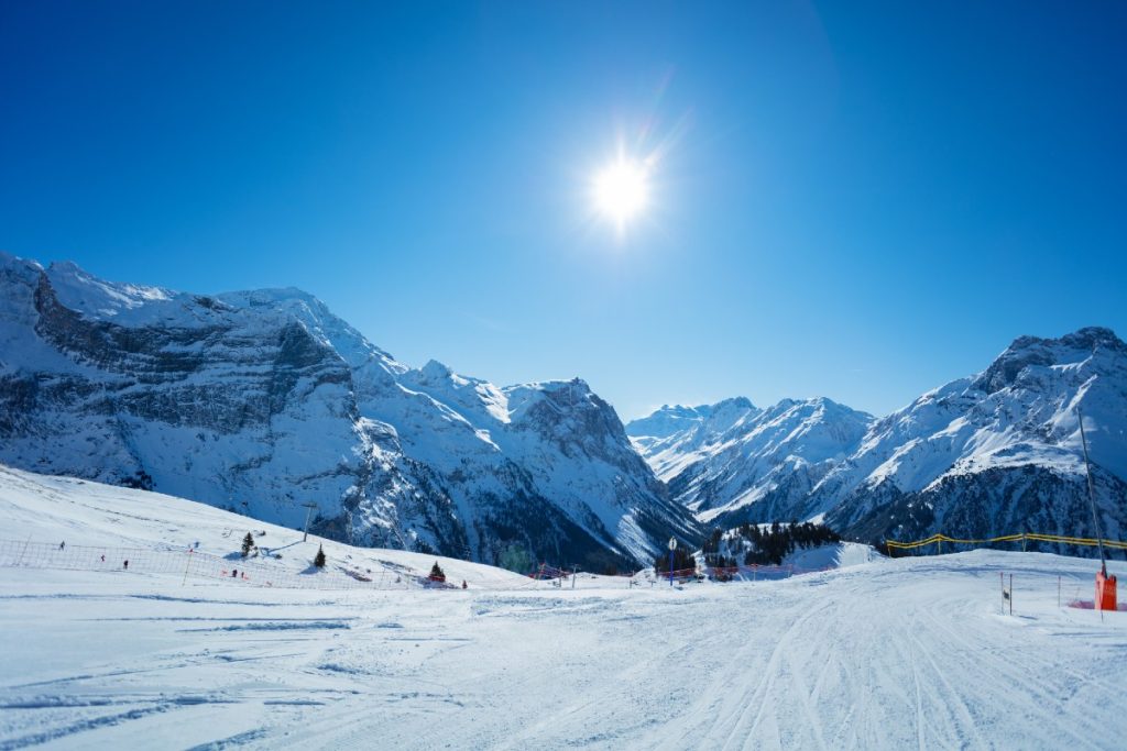 Eine Skipiste im Vordergrund, Berge unter blauem Himmel im Hintergrund