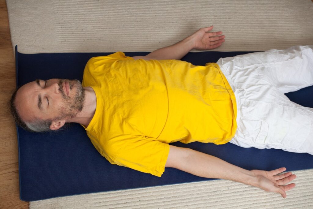 Mann mit geschlossenen Augen auf Fitnessmatte und Teppich liegend