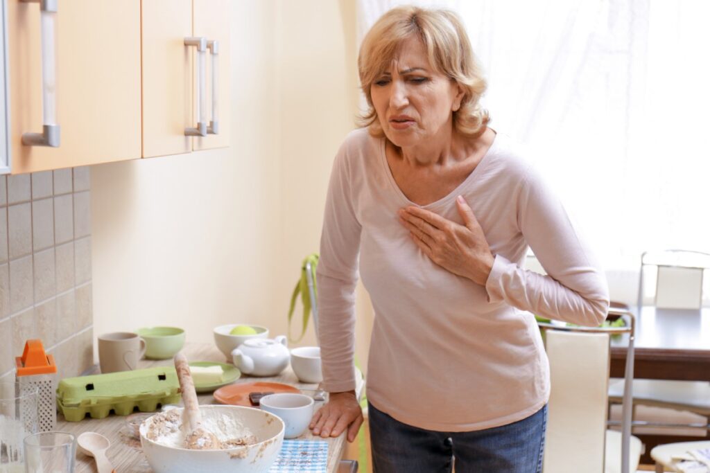 Ältere Frau, die sich mit schmerzverzerrtem Gesicht in der Küche die Hand an die Brust hält