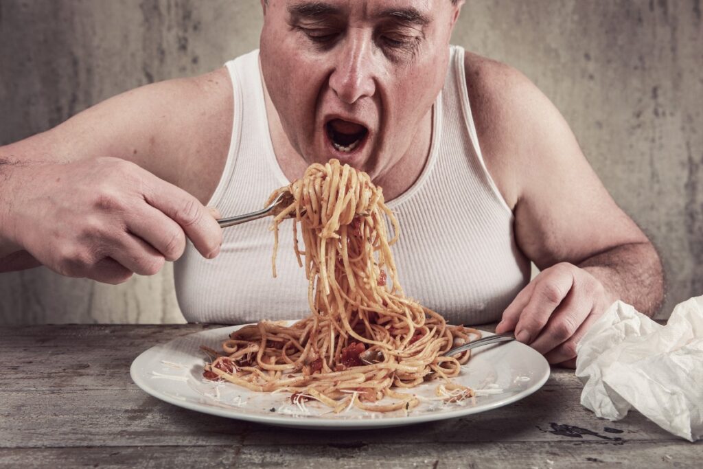 Älterer Mann in Unterhemd, der eine große Portion Spaghetti in sich hineinschaufelt