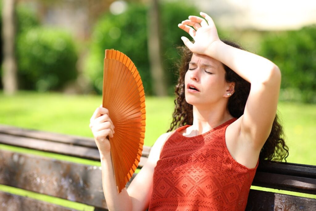 Frau mit Fächer in Hitze auf Parkbank