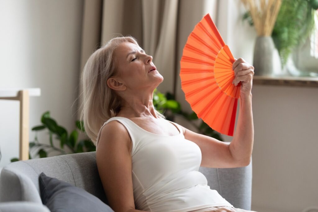Frau in Hitzewallung mit Fächer auf Couch