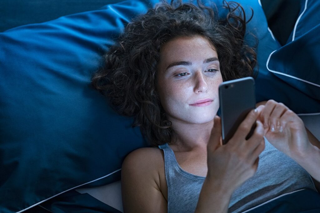 Frau, die abends im Bett auf Ihr Handy schaut