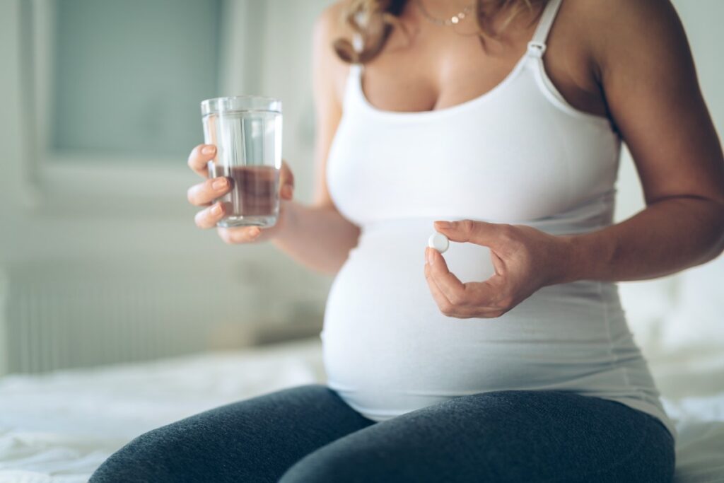 Schwangere Frau mit einem Glas Wasser und einer Tablette in der Hand