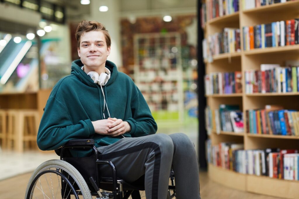 Junger Mann im Rollstuhl vor Bücherregalen