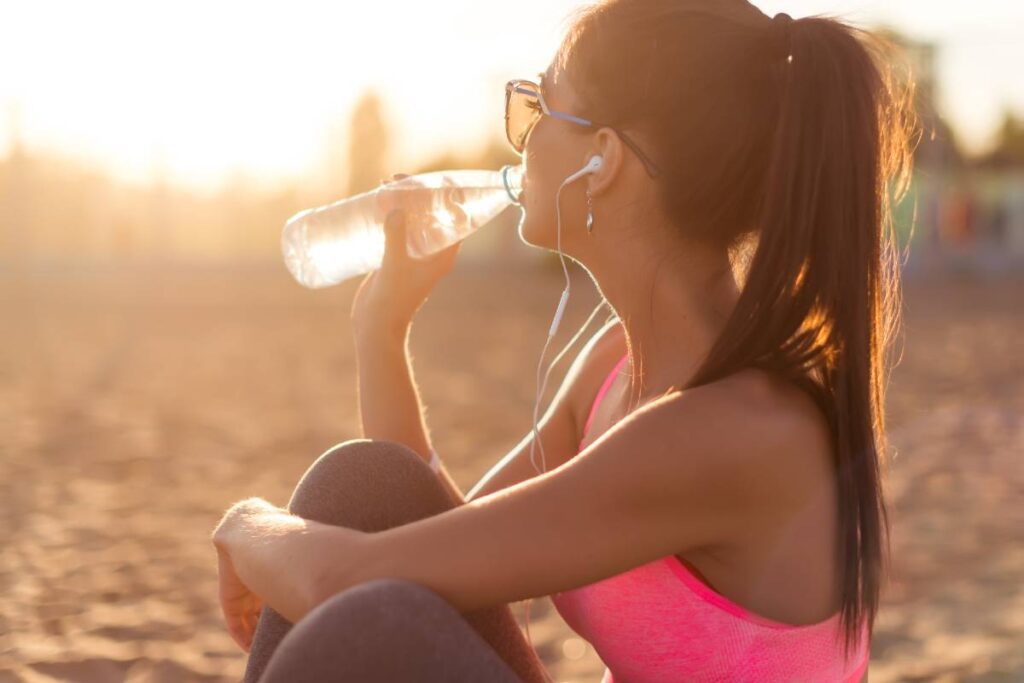 Sportliche Frau trinkt draussen Wasser
