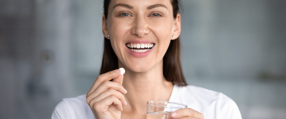 Lachende Frau mit Pille und Wasserglas in der Hand