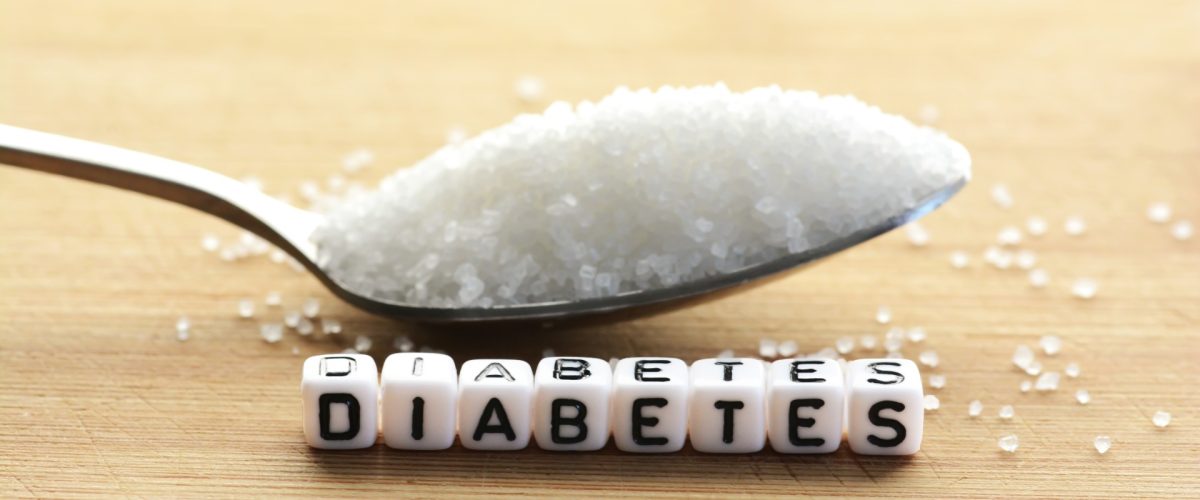 Ein Esslöffel Zucker über dem Schriftzug Diabetes, der aus beschrifteten Steinchen besteht