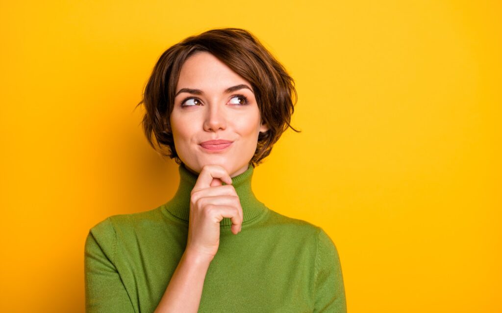 Frau, die verschmitzt mit der Hand am Kinn nach oben schaut