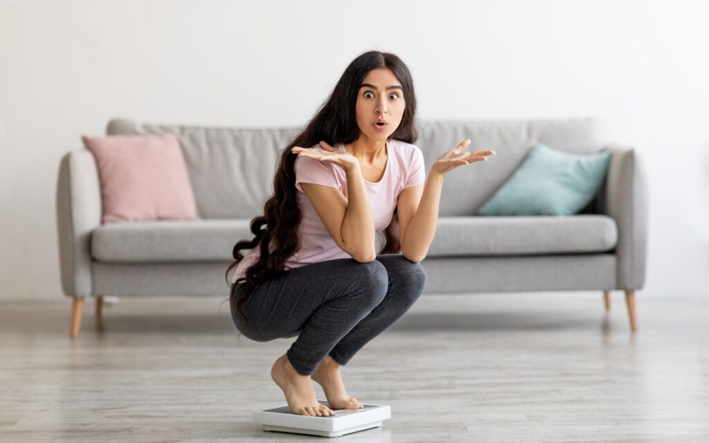 Überraschte junge Frau auf Waage