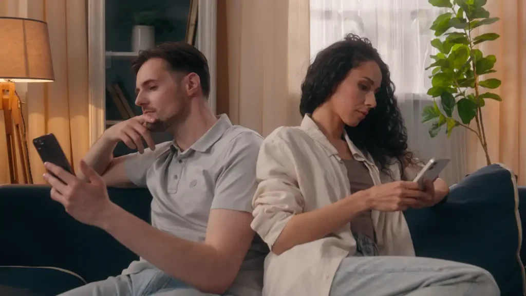 Pärchen sitzt von einander abgewandt mit Handys auf der Couch