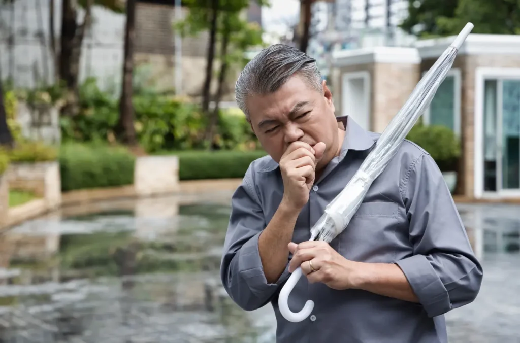 Älterer asiatische Mann mit regenschirm muss husten