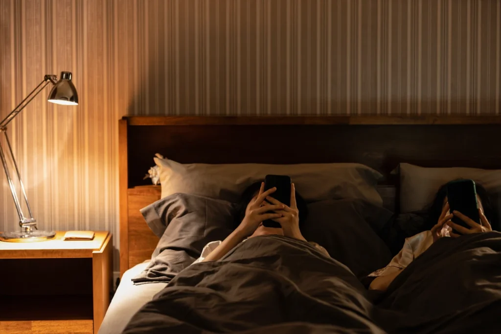 Ehepaar schaut getrennt Handy im Bett