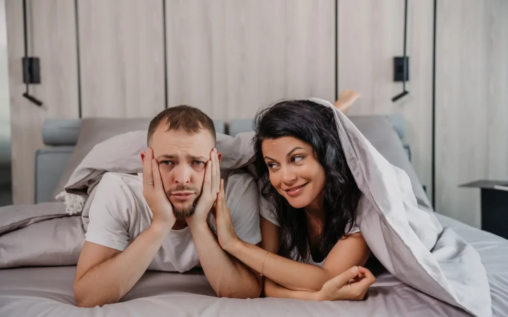 Paar im Bett, er frustriert, sie aufmunternd