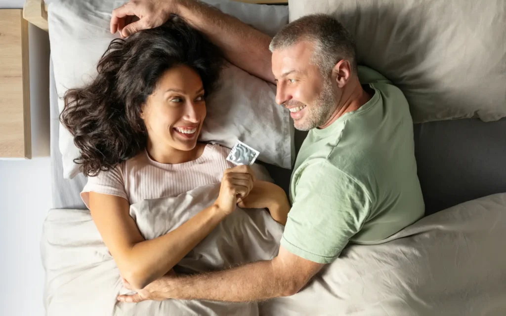 Reiferes Pärchen mit Kondom lächelnd im Bett