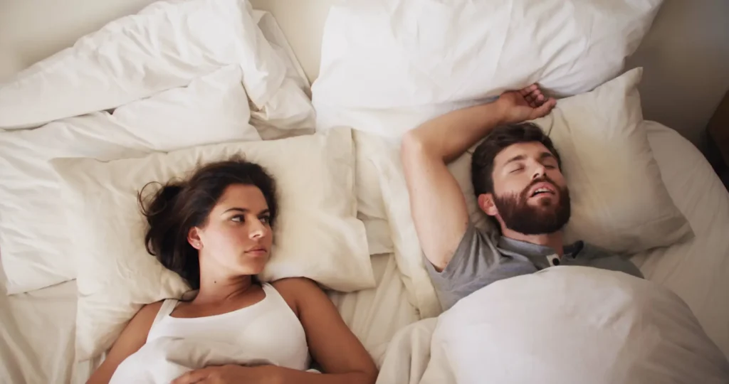 Paar im Bett und Frau kann wegen seinem Schnarchen nicht schlafen