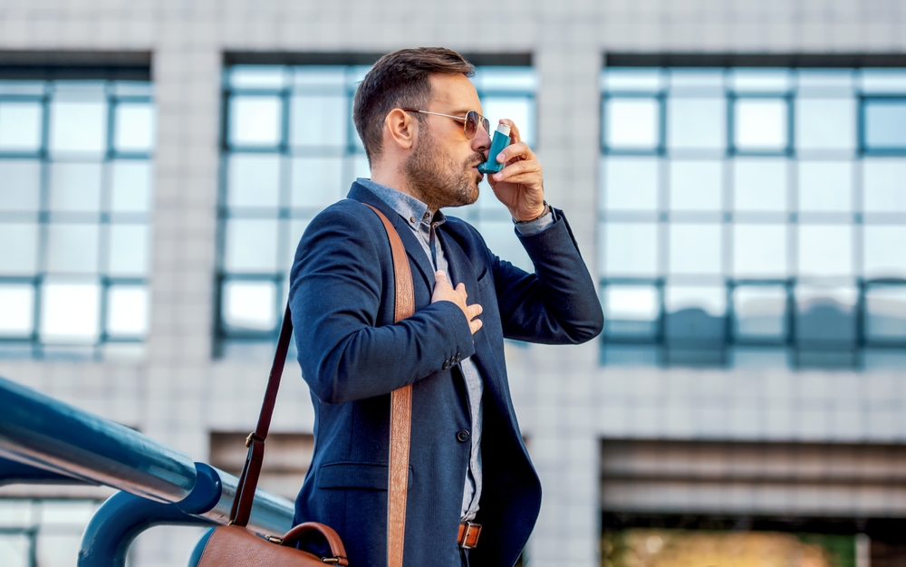 Jeune homme souffrant d’asthme utilisant un inhalateur pour soulager une crise respiratoire dans un contexte de stress.