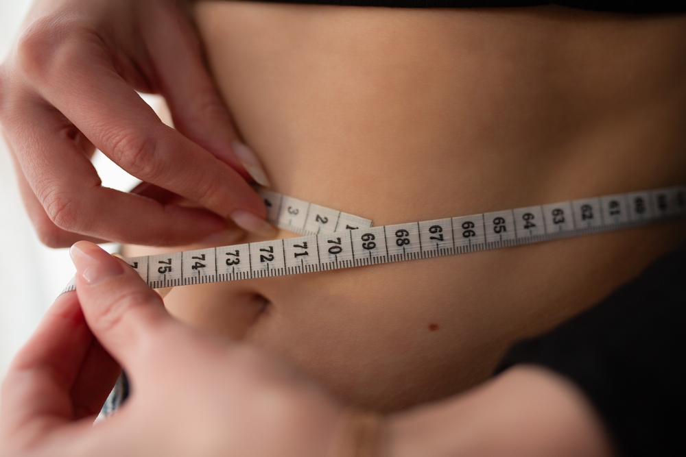 Jeune femme en gros plan mesurant son tour de taille avec un mètre ruban blanc