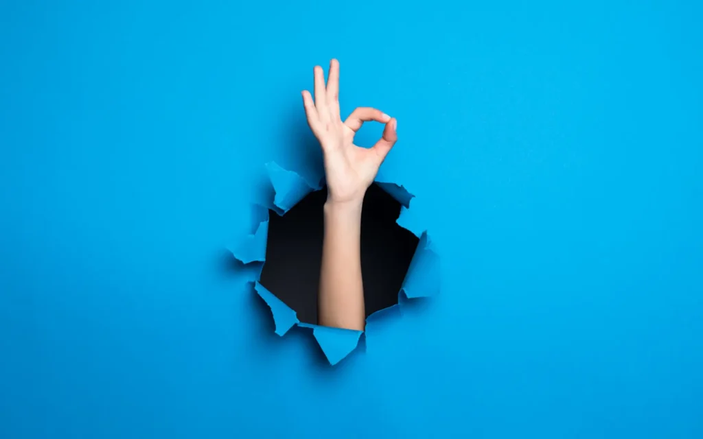 Hand bricht aus blauer Wand hervor und gibt ein Alles Okay zeichen