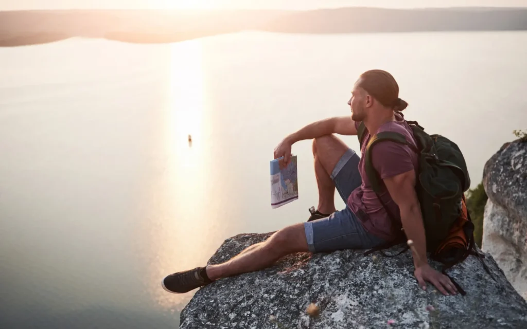 Mann blickt entspannt von einem Felsen über einen See