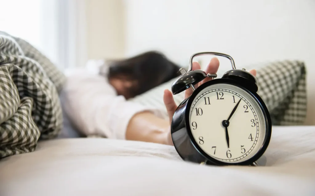 Person schläft im Bett während Wecker im Vordergrund steht