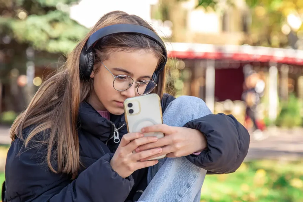 Teenager Mädchen mit Kopfhörern auf schaut auf ihr Handy