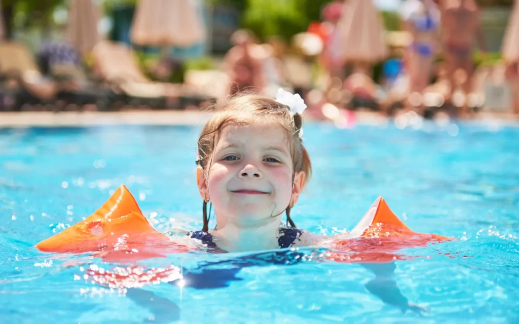 Kleines Mädchen mit Schwimmflügeln im Freibad