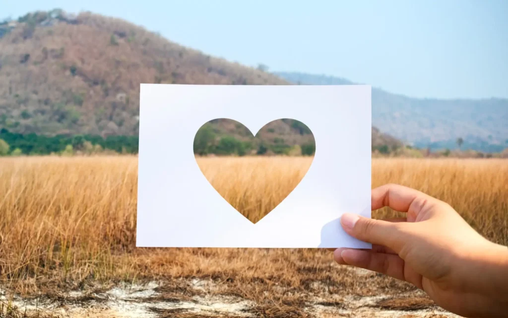 Blatt Papier mit ausgeschnittenem Herz vor eine Landschaft