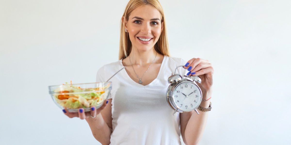 Junge Frau mit Schüssel voll Salat und Wecker in den Händen