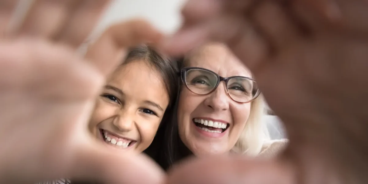 Oma und Enkelin machen lächelnd das Herzzeichen mit den Händen
