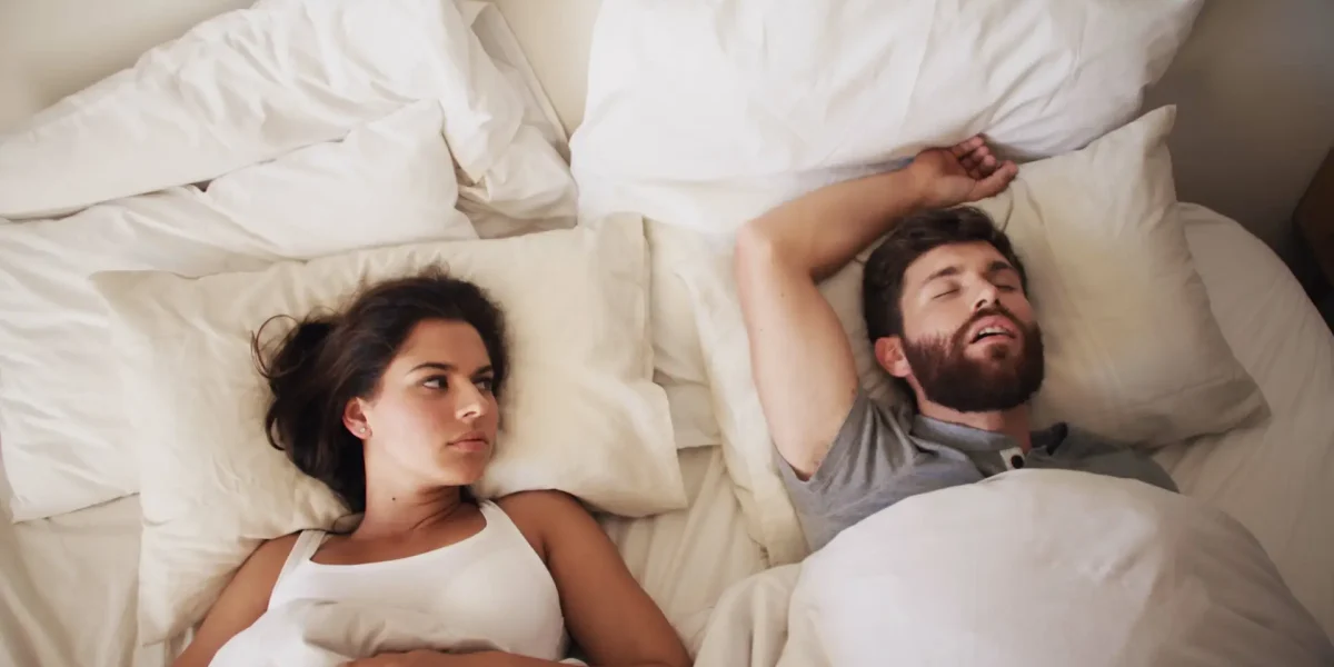 Paar im Bett und Frau kann wegen seinem Schnarchen nicht schlafen