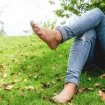 Person in Jeans liegt barfuss auf dem Gras und entspannt