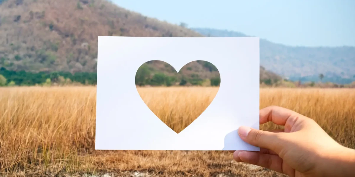 Blatt Papier mit ausgeschnittenem Herz vor eine Landschaft