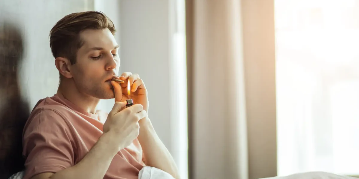 Junger Mann raucht Cannabis im Bett