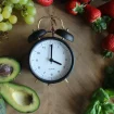 Wecker inmitten von Lebensmitteln als Symbol für Chrononutrition