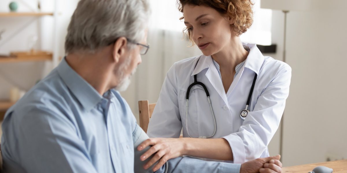 Junge Frau Doktorin mit weißer Uniform, mit Stethoskop zur Kontrolle des reifen Blutdrucks eines Patienten bei der Sitzung im Krankenhaus.