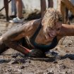 Frau, die bei einem sportlichen Wettbewerb lachend durch den Schlamm robbt