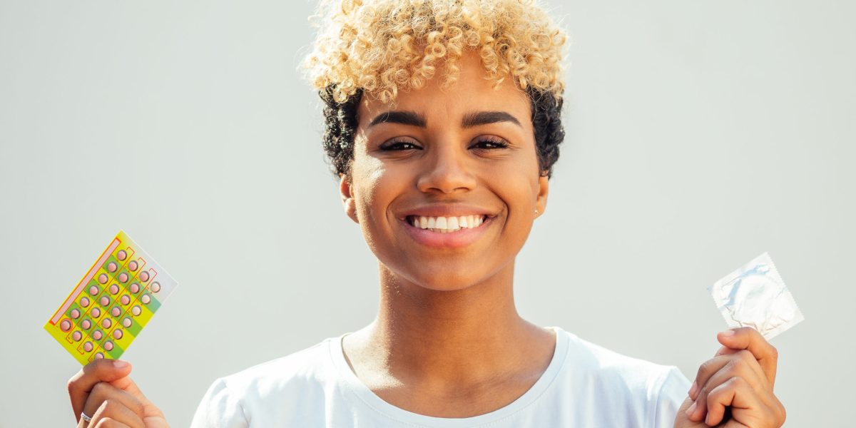Femme tenant une plaquette de pilules contraceptives dans une main et un préservatif dans l’autre, représentant différentes méthodes de contraception.