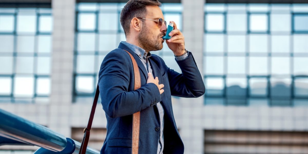 Jeune homme souffrant d’asthme utilisant un inhalateur pour soulager une crise respiratoire dans un contexte de stress.
