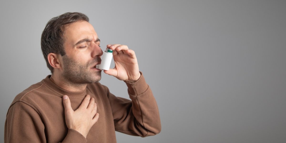 Homme utilisant un inhalateur pour l’asthme bronchique, illustrant la gestion quotidienne de la respiration et des symptômes.