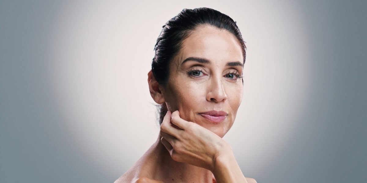 Femme mature appliquant une routine de soins anti-âge en studio, illustrant la santé et l’hydratation de la peau à la ménopause.