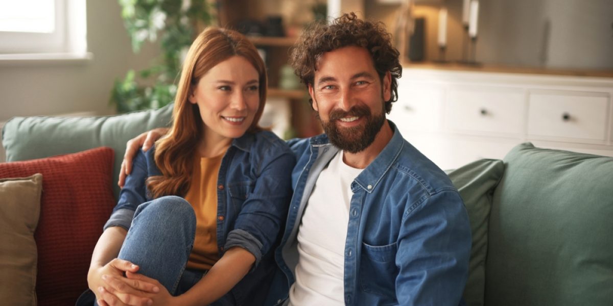 Couple souriant et amoureux assis sur un canapé en mode cocooning, illustrant la santé sexuelle et le bien-être intime en 2026.
