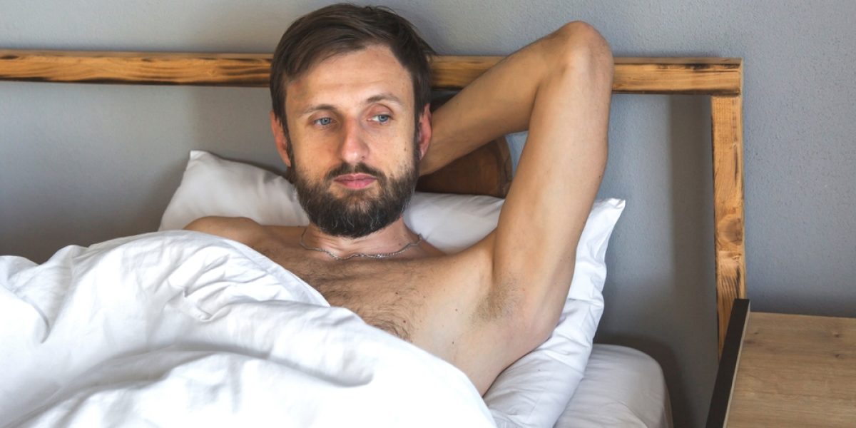 Homme pensif dans son lit, main derrière la tête, réfléchissant à sa santé intime et sa libido masculine, crise de la quarantaine et bien-être masculin.